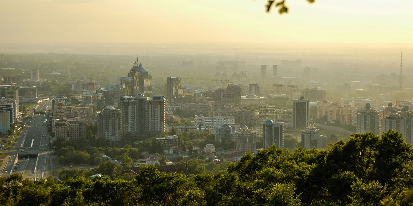 A scenic cityscape view at sunset, with high-rise buildings and lush green trees below.