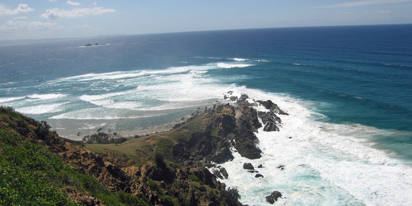 Image of Byron Bay's Main Beach with the rough waves crashing the rocky shores