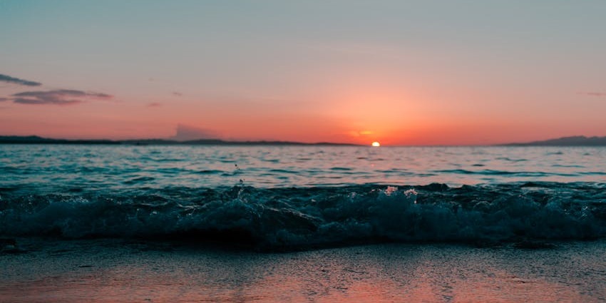 An image of a beach at Sunset on the horizon reflecting over calm waves, resembling the Sunset at Rose Hill, Mauritius.