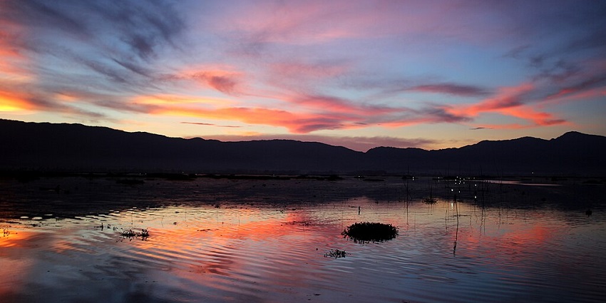 The floating lake in Manipur in the evening with a vibrant, colorful sky, sunset and reflections.