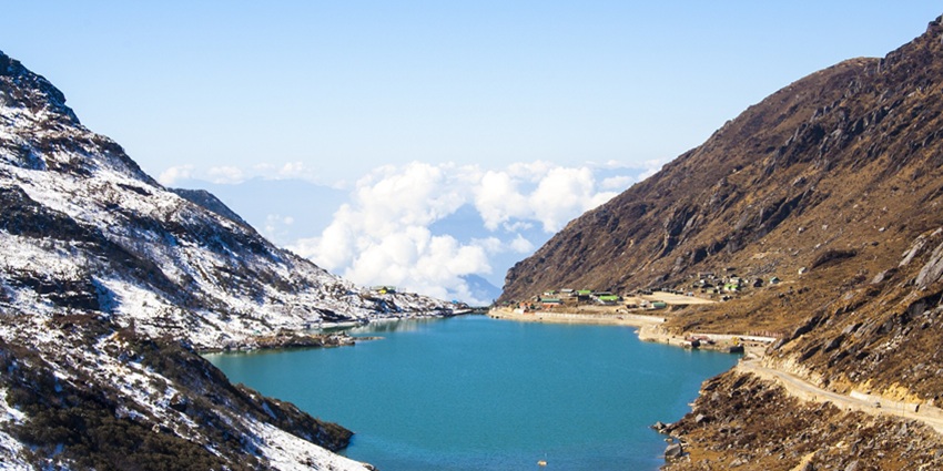 Tsomgo lake with a small water body surrounded by snowy, sandy shorelines and mountains