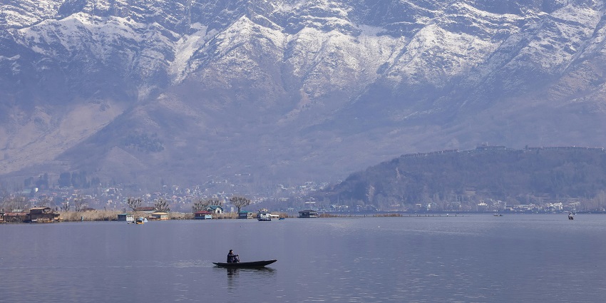 A view of a Lake in Kashmir with a lone shikara boat being rowed, against the mountains