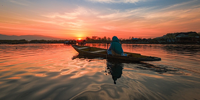 Dal lake with a large still water body, a woman on a wooden boat and a vibrant sunset