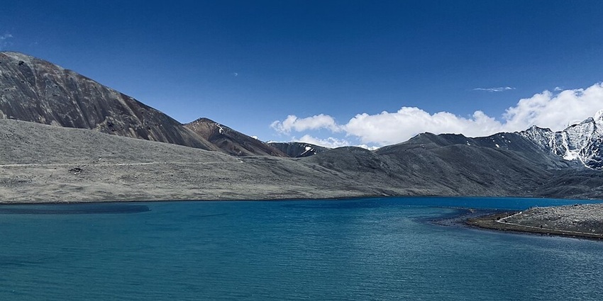 Gurudongmar lake with a blue water body, sandy shorelines and snowy mountain peaks