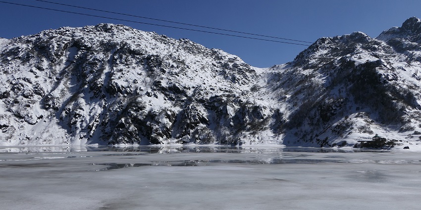 Tsomgo Lake with a frozen water body surrounded by white snowy mountains and wires