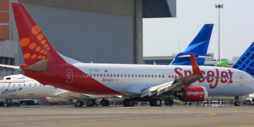 Multiple commercial aircraft parked on the runway of an airport with building in the back