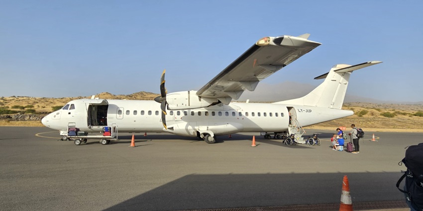 Big white propeller engine aeroplane with a luggage trolley near the aeroplane and people