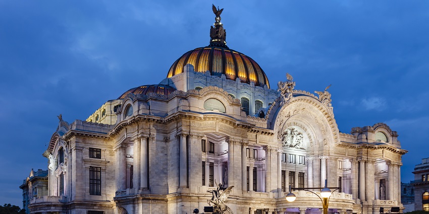 Structure of Palacio de Bellas Artes illuminated at night with people sitting in the complex