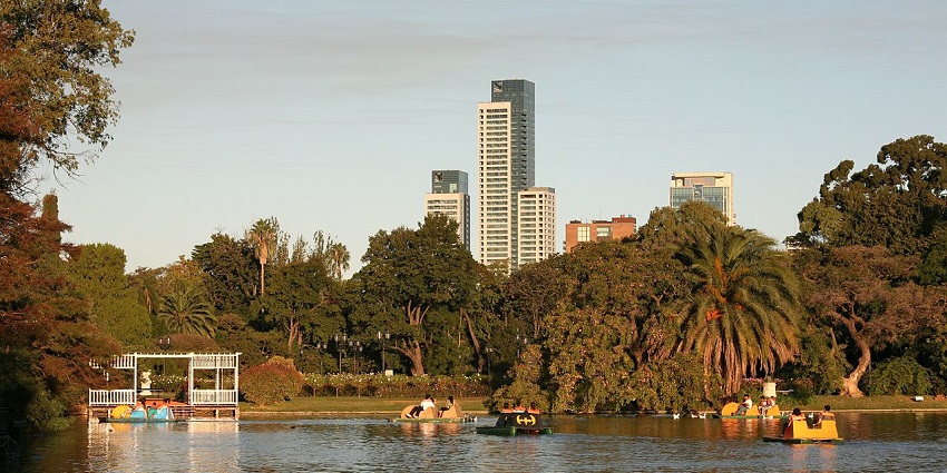 Boating in the lake of Palermo Rose Garden is surrounded by lush greenery and buildings.