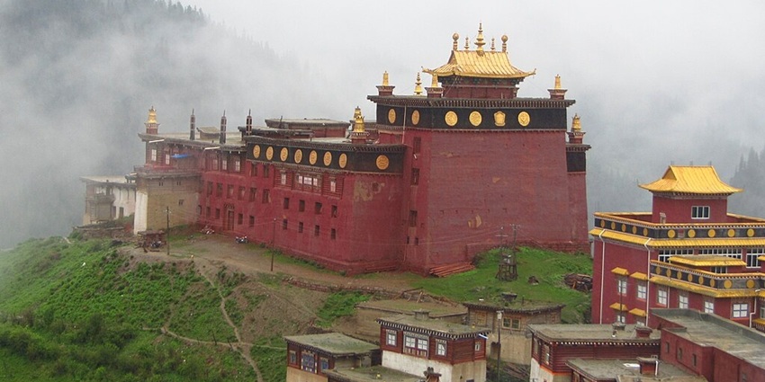 An image of a large, red Tibetan Palpung monastery with golden roofs, surrounded by misty mountains and green hills.