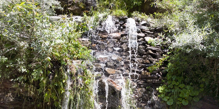 Waterfall cascades down leafy green mountains, creating a serene and breathtaking view