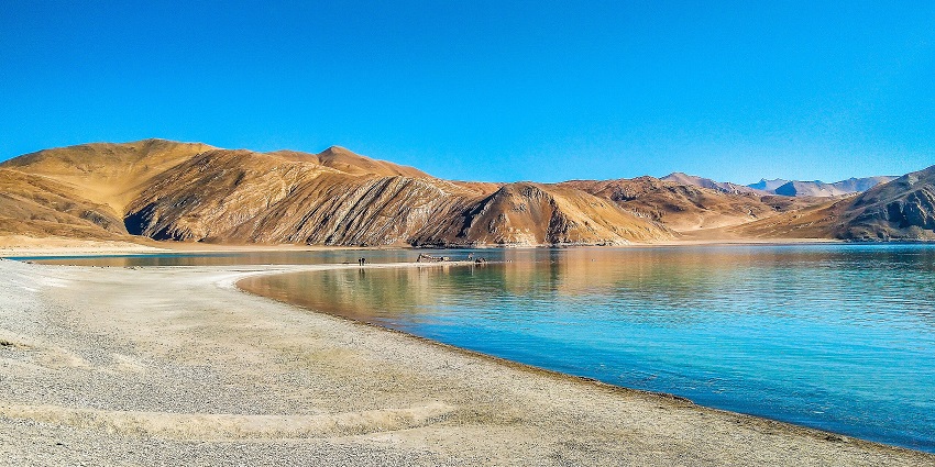 Pangong Lake’s deep blue expanse stretches between arid and golden-brown mountains.