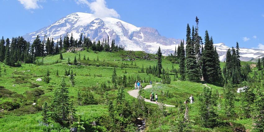 An image of snow covered mountain peaks and people walking on the road
