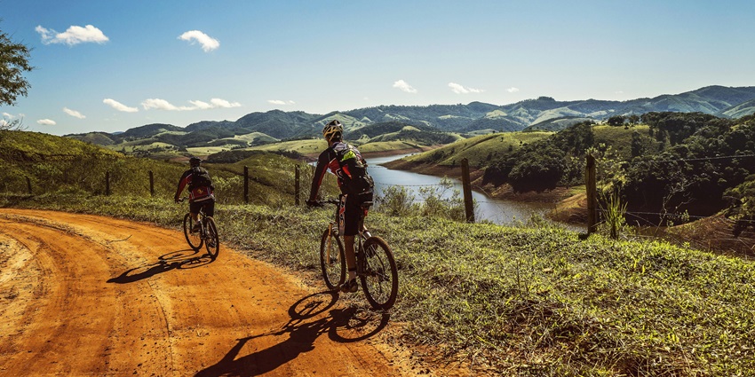 Cyclist riding along a riverside road surrounded by trees and natural landscape