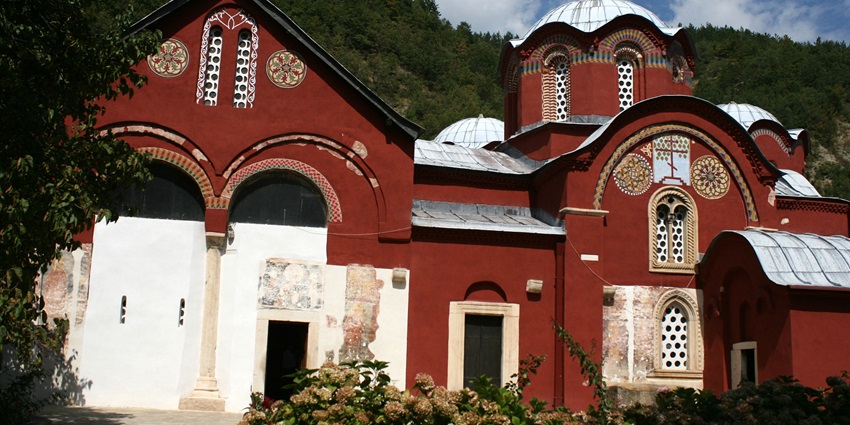 Scenic view of the Patriarchate of Peć in Kosovo, highlighting its red facade, domes, and mountains, one of the best places to visit in Kosovo.