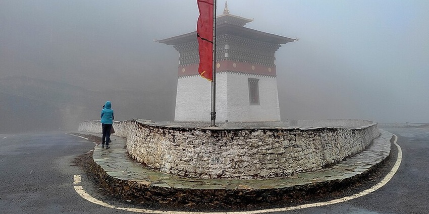 An image of a foggy pathway of the Pele La Pass, leading to a traditional white Bhutanese stupa with a red band