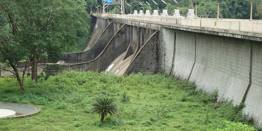 A panoramic view of Peringalkuthu Dam with calm waters and misty hills in the background.