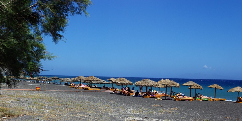 A scenic view of Perissa Beach, one of the black sand beaches in the world, featuring black sand and the Aegean Sea.