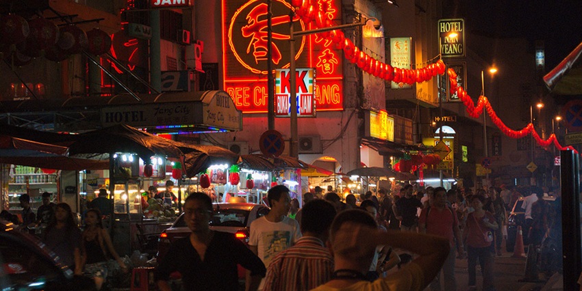 Bustling night market in Kuala Lumpur with lanterns, neon signs, and street food stalls.