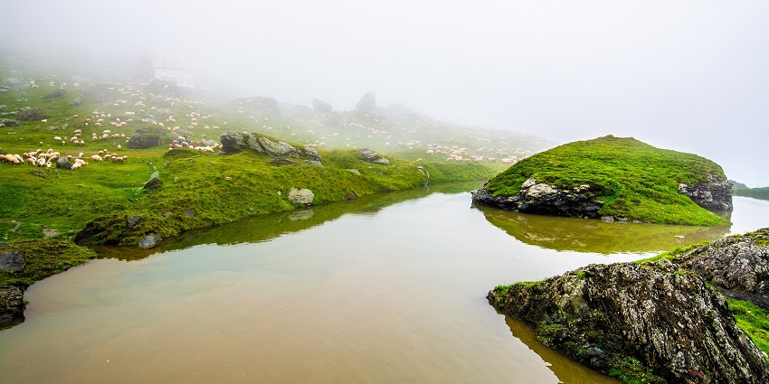 A misty mountain lake reflecting the cloudy sky, creating a tranquil and ethereal atmosphere.