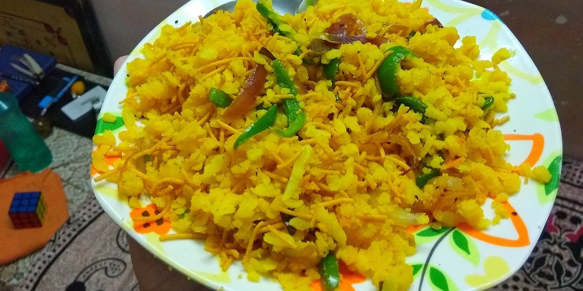 An image showing Indori Poha served with sev, pomegranate, and spices on a plate among the healthy street food in India.