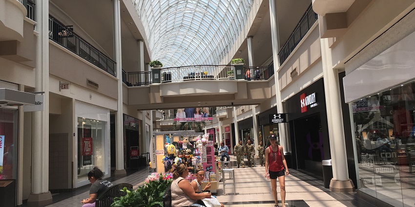 Spacious mall with a transparent roof, sunlight streaming in, and a crowd of shoppers inside