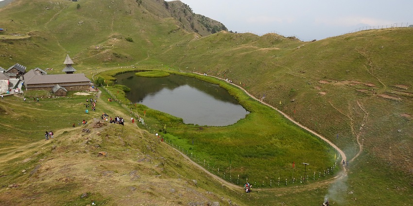 Prashar Lake with its floating island, encircled by misty mountains under a cloudy sky.
