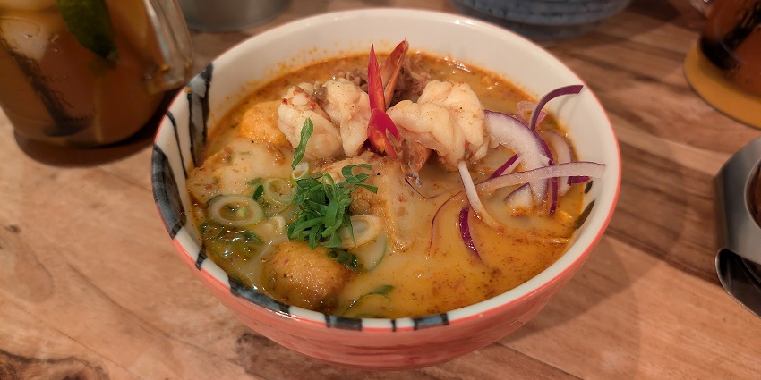 Prawn laksa dish with prawn, thinly sliced onions and coriander leaves in noodle soup