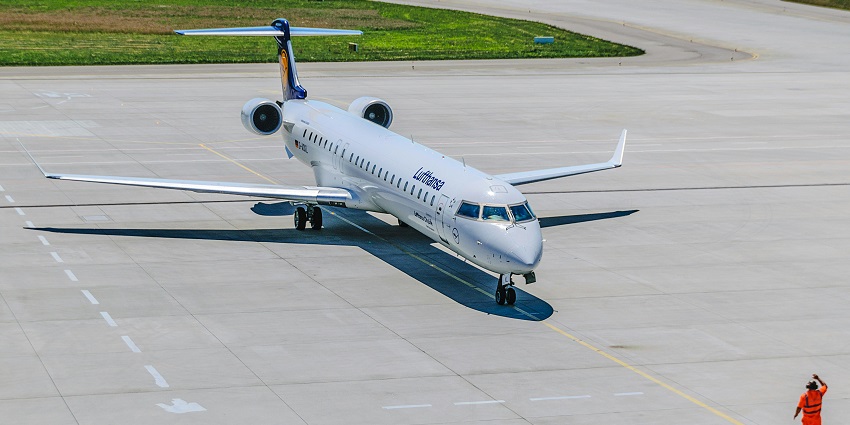 A person stands in front of an airplane on the tarmac, facing away from the camera