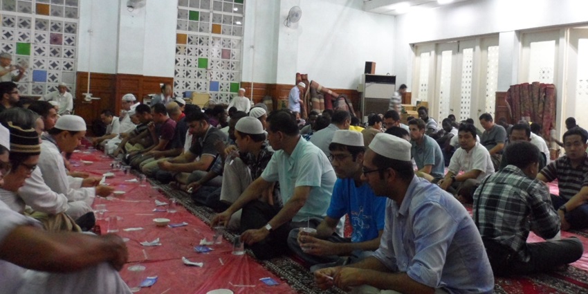 An image of multiple muslim individuals sitting together in order waiting for food