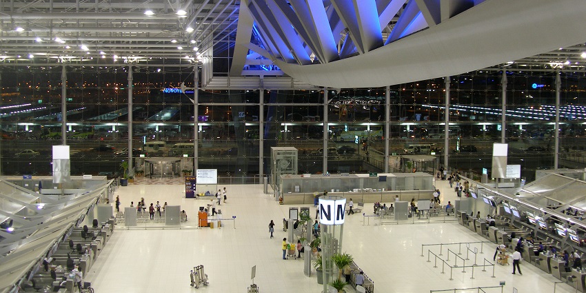 Bustling airport terminal with numerous passengers, check-in counters, and departure gates.