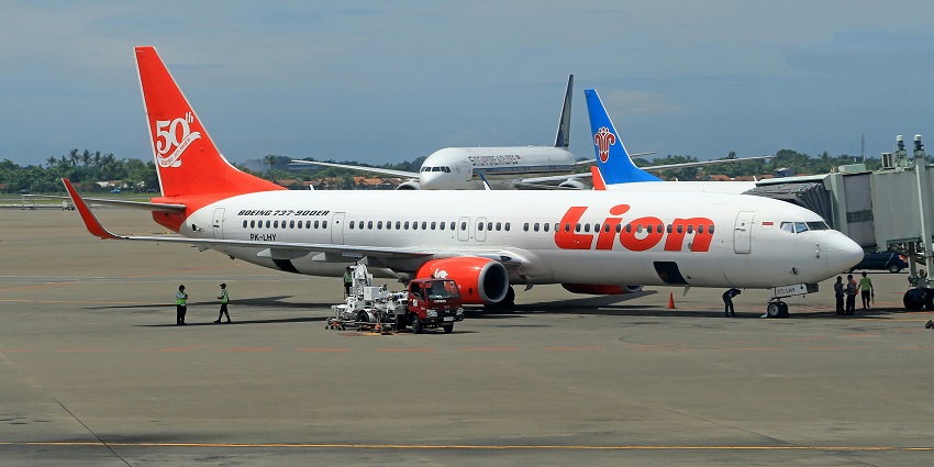 Multiple aeroplanes parked near the passenger boarding bridge and airport staff near them