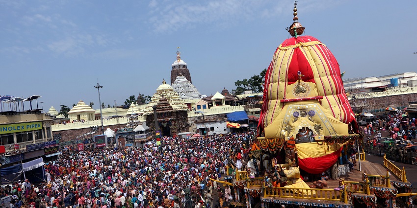 An image of a decorated chariot in front of a temple, surrounded by a crowd during Ratha Yatra.