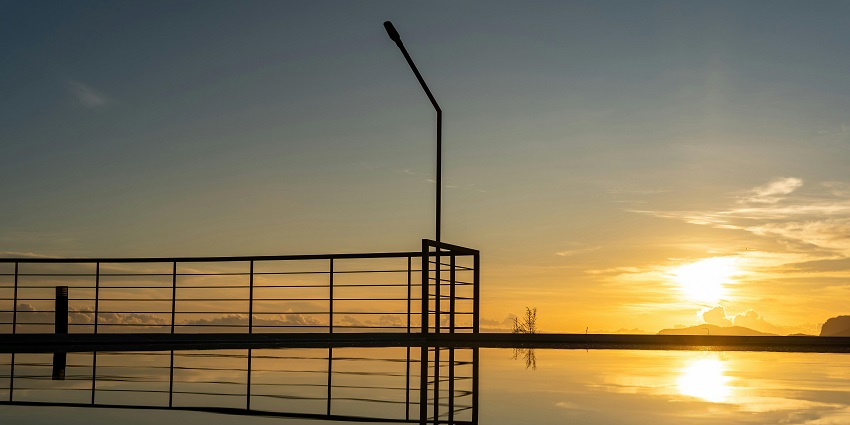 Golden sunrise reflects on a still lake, framed by a wooden fence along the tranquil shore