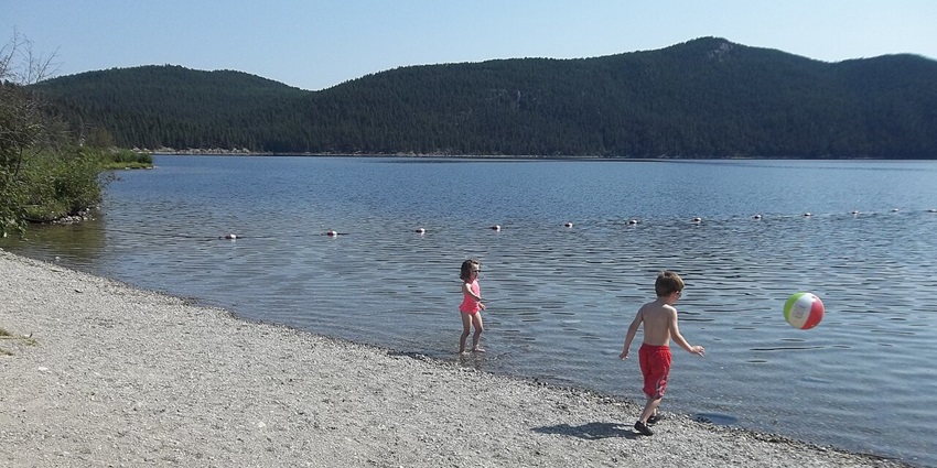 Sunny lakeside beach with gentle waves, families on picnic blankets, and children playing in the sand at Forest Lake Beach.