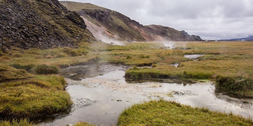 An image of a natural hot spring bubbling in foreground, observed by spectators, resembling the hot springs in Paro