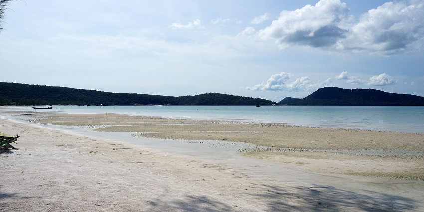 An image of the Saracen Bay, with a sandy shore, clear waters, forested hills, and peaceful skies.
