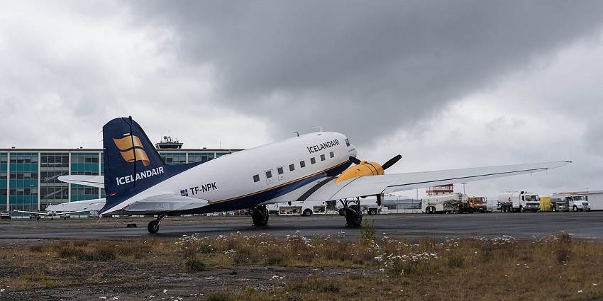 An aircraft is parked at Reykjavík Airport with a cloudy sky and urban surroundings.
