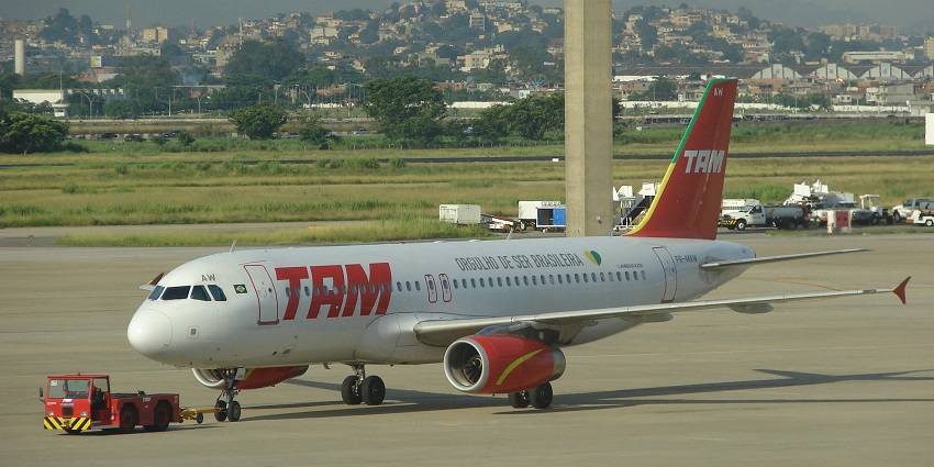TAM Airbus aircraft parked at Galeão Airport with terminal buildings in the background.