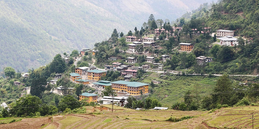 An image of a village in Bhutan amidst hills, featuring terraced greenery and dense vegetation