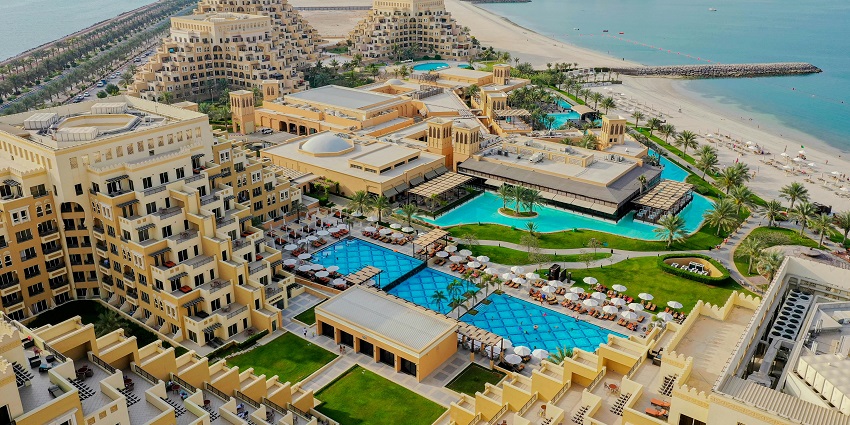 An aerial view of a resort with unique pyramid-like buildings, pools, and a sandy beach