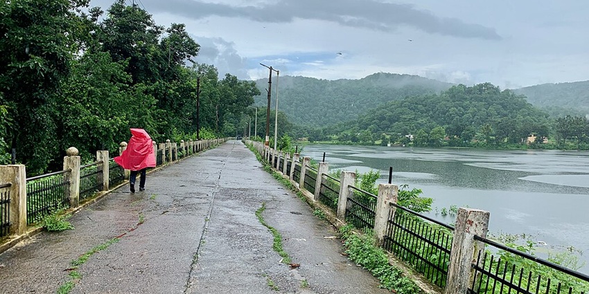 Lake with a large water body, iron fences and a person in a red raincoat on the pathway
