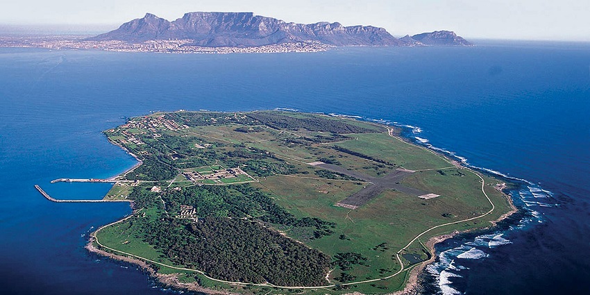 An image of Robben Island in South Africa, showing greenery, buildings and ocean waves.