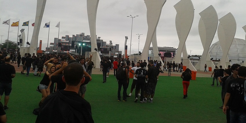 An image of a crowd gathers on a green field with white sculptures, under a cloudy sky.
