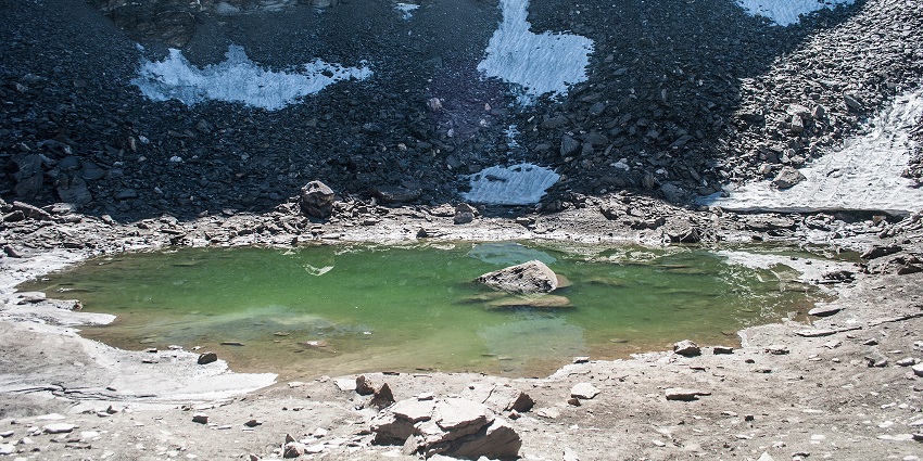 Roopkund lake with a small and greenish water body surrounded by rocky shorelines
