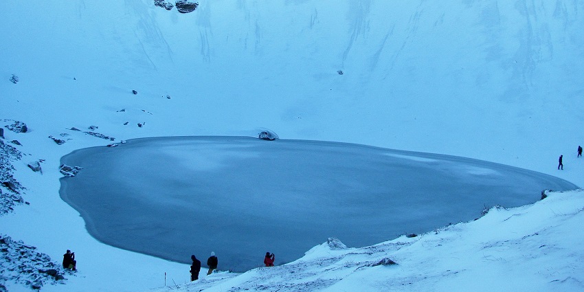 Frozen Roopkund surrounded with snow, and people exploring the snow-covered land