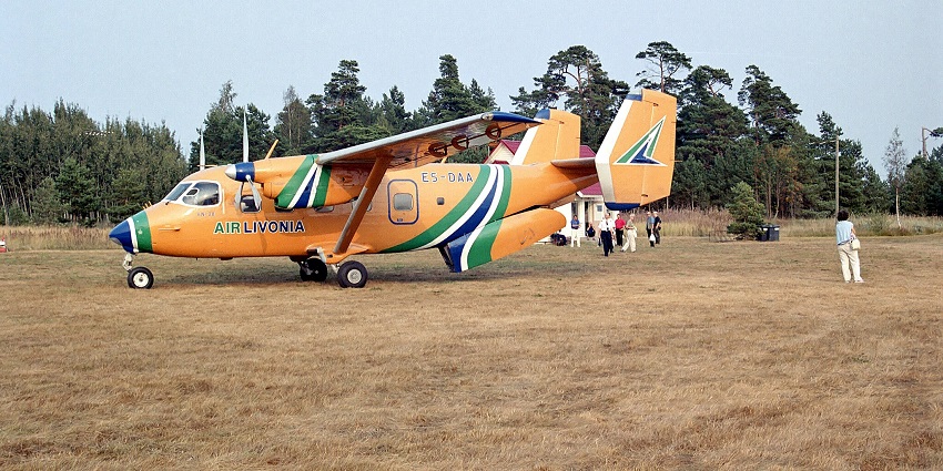 An An-28 aircraft of Air Livonia is parked at Ruhnu airfield under a clear sky and trees