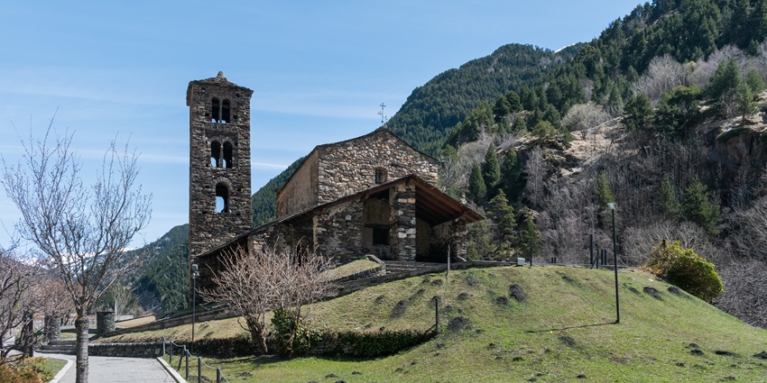 Sant Joan de Caselles, a Romanesque stone church with a tall bell tower in a green valley.