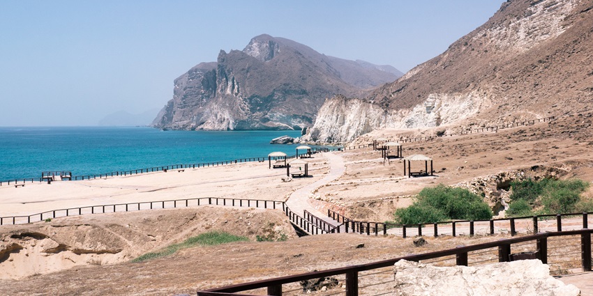 A view of a serene coastal town at dusk, featuring palm trees a sandy beach at Salalah.