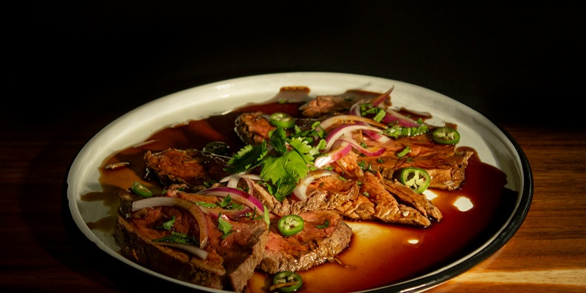 An image showing a close-up of a juicy steak beef bagel served on a dinner plate.
